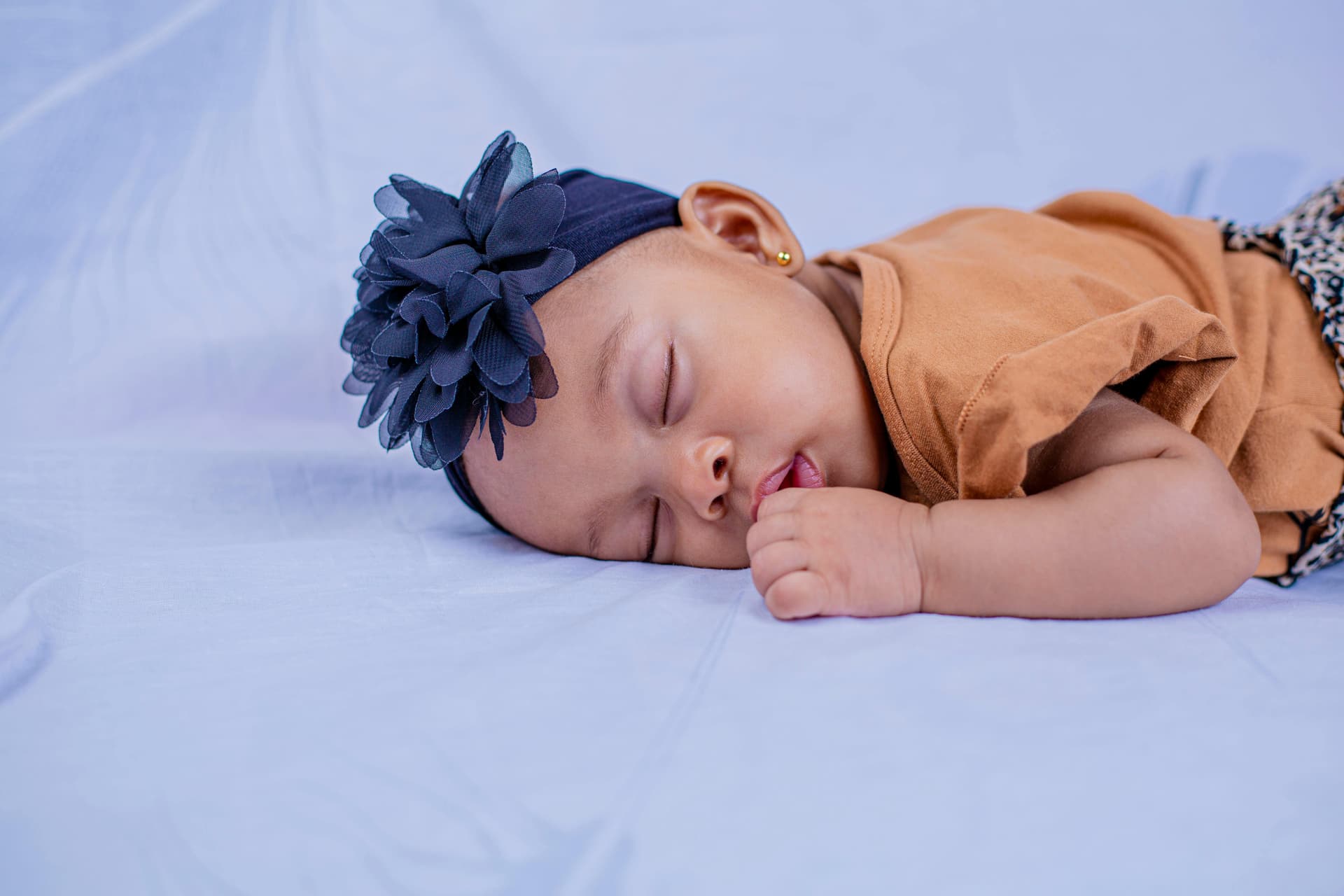 Bebé dormido acostado sobre una tela clara, con una diadema floral.