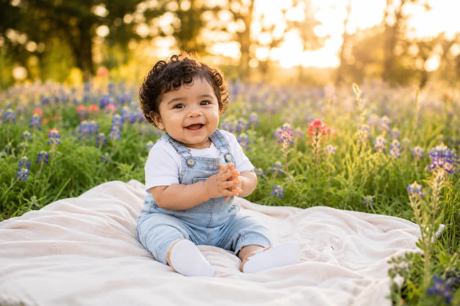 Bebé niña sentada en un jardín con las primeras flores de primavera y ramas de cerezo en flor al fondo